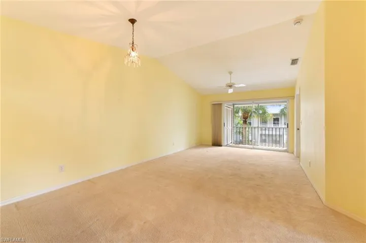 Unfurnished dining and living room, featuring light carpet, vaulted ceiling, suspended lighting, and ceiling fan