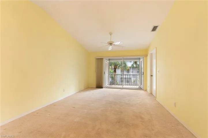 Empty room with a ceiling fan, vaulted ceiling, and light carpet