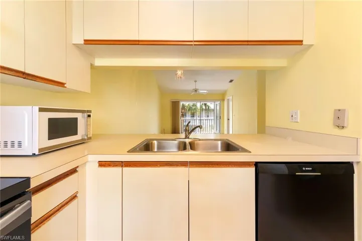 Kitchen with black dishwasher, white microwave, range, light countertops, and white cabinets