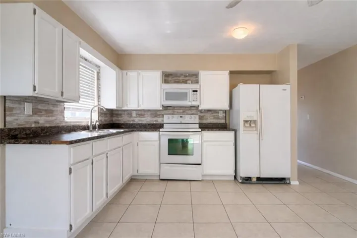 Kitchen with dark countertops, white appliances, white cabinets, and decorative backsplash