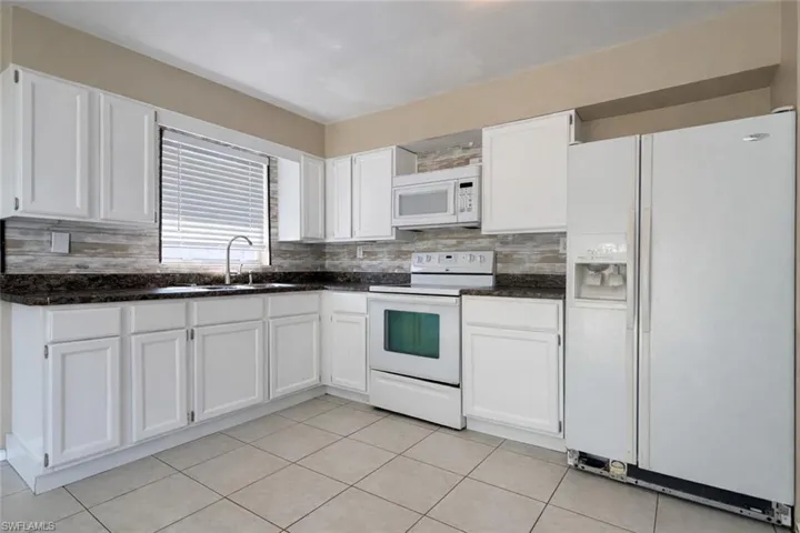 Kitchen with white appliances, white cabinets, backsplash, and dark stone countertops