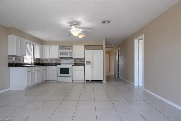 Kitchen with white appliances, white cabinetry, decorative backsplash, and light tile patterned flooring