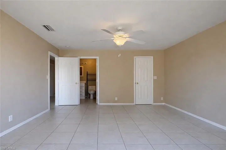 Unfurnished bedroom with ensuite bathroom, ceiling fan, and light tile patterned floors