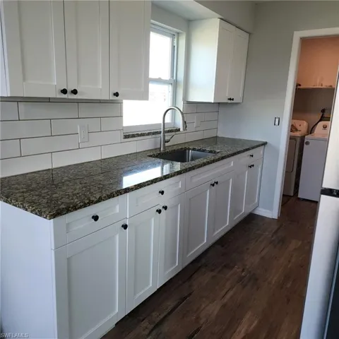 Kitchen with independent washer and dryer, dark hardwood / wood-style floors, dark stone countertops, white cabinets, and sink