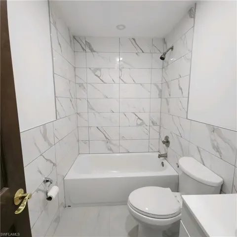 Full bathroom with tile walls, tile flooring, tiled shower / bath combo, and toilet