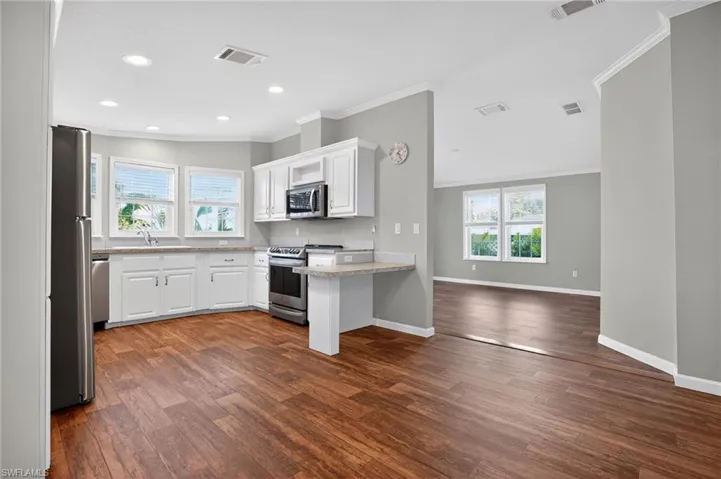 Kitchen with white cabinets, crown molding, stainless steel appliances, dark wood-style flooring, and recessed Lights!