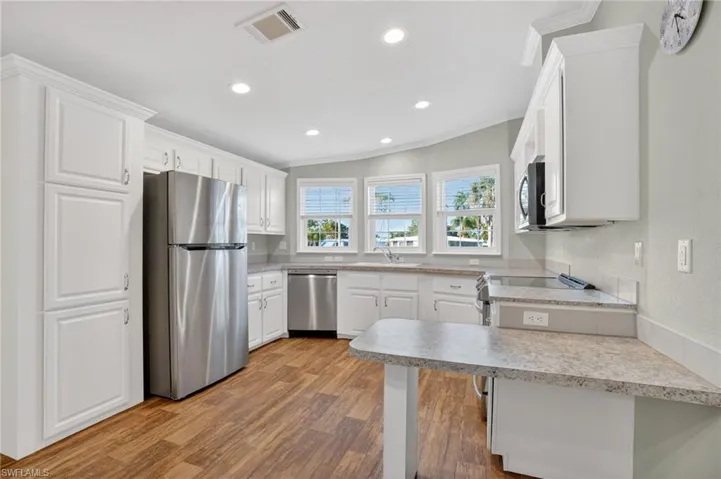 Kitchen featuring white cabinets, a peninsula, stainless steel appliances, light countertops, and vaulted ceiling