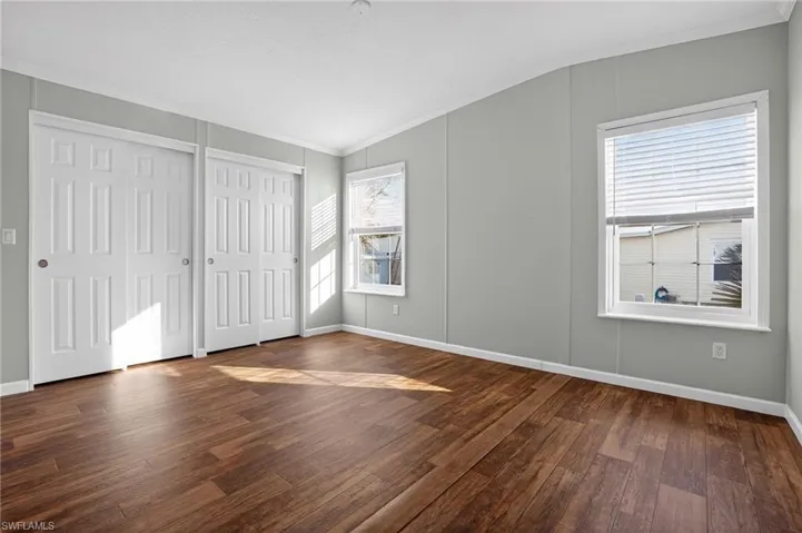 Primary bedroom featuring crown molding, multiple closets, and dark wood-type flooring