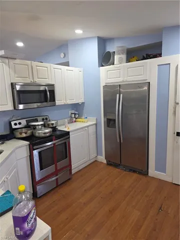 Kitchen featuring stainless steel appliances, dark wood-type flooring, white cabinets, and light stone counters