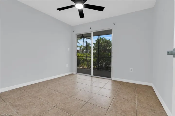 Spacious room featuring neutral paint, tile flooring, a black ceiling fan, and sliding glass doors opening to a screened outdoor area with abundant tropical foliage