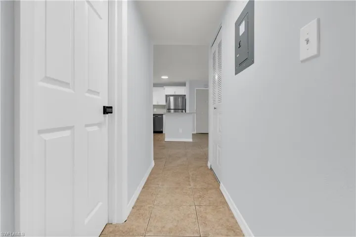 Hallway featuring neutral wall paint, tile flooring, white panel doors with black hardware, and a louvered closet door