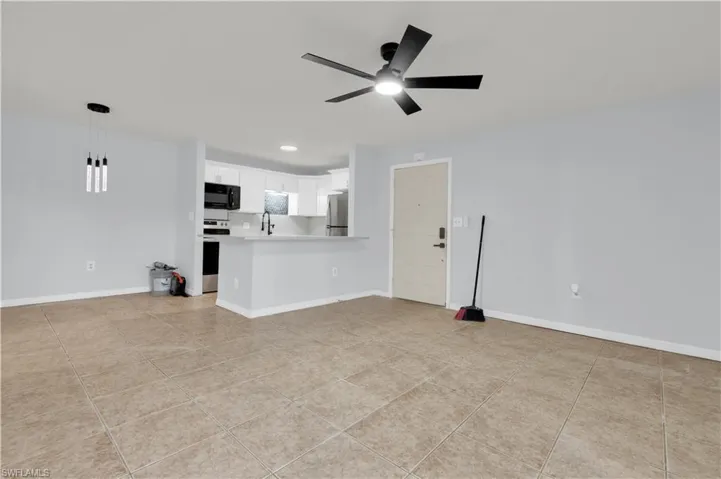 Open-concept living area with large format tile flooring, a modern ceiling fan, and a kitchen featuring white cabinetry, dark appliances, and a breakfast bar