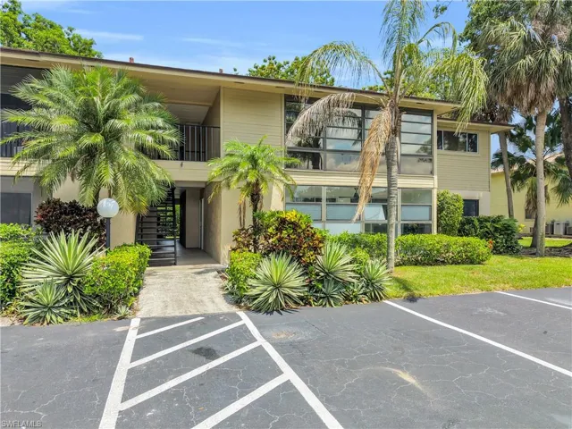 Multi-level building exterior featuring a neutral facade, large windows, and established tropical landscaping