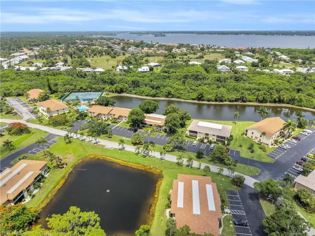 Aerial perspective showcasing a residential community with multiple buildings, two distinct ponds, and a large body of water in the distance