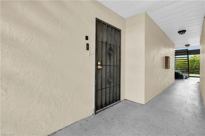Entryway featuring a wrought iron security gate, textured stucco walls, a concrete walkway, and a slatted white ceiling