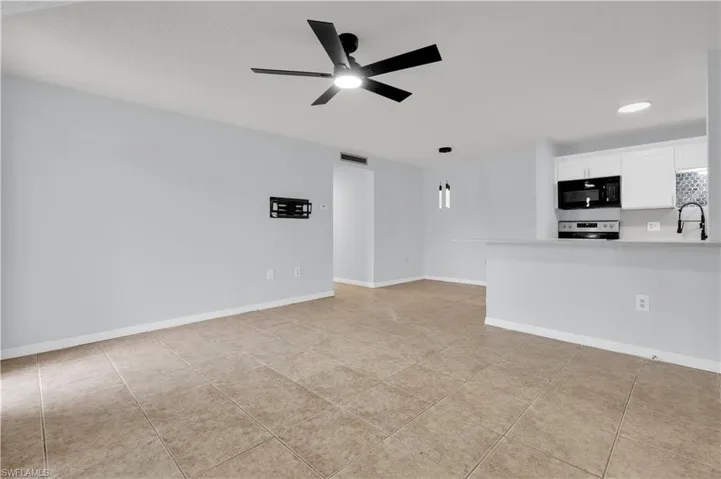 Open-concept living space with tile flooring throughout, a modern black ceiling fan with integrated lighting, and a kitchen featuring white cabinetry, black appliances, and a mosaic tile backsplash
