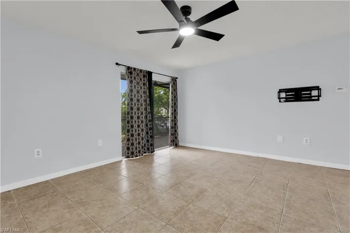 Spacious room featuring neutral-toned tile flooring, a modern ceiling fan with integrated lighting, and a wall-mounted bracket