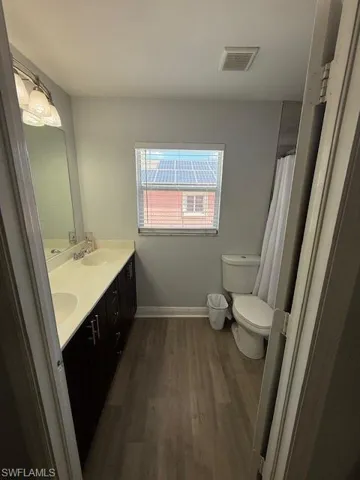 Full bath featuring double vanity, curtained shower, and dark wood finished floors