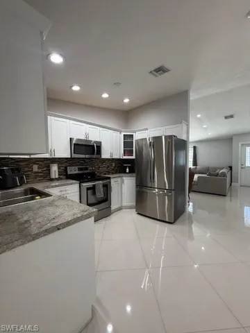Kitchen with stainless steel appliances, white cabinets, glass insert cabinets, tasteful backsplash, and recessed lighting