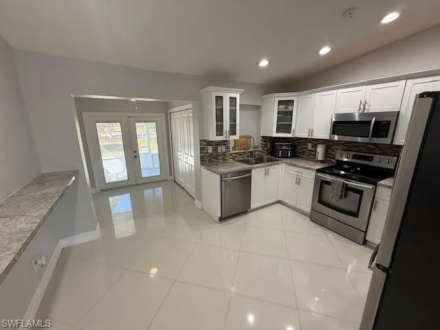 Kitchen with stainless steel appliances, white cabinetry, vaulted ceiling, recessed lighting, and backsplash