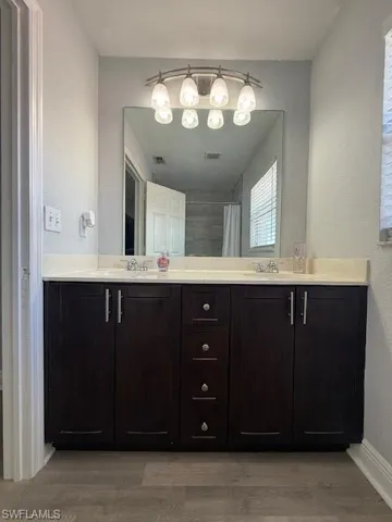 Full bath with a textured wall, double vanity, light wood-type flooring, and a shower with curtain