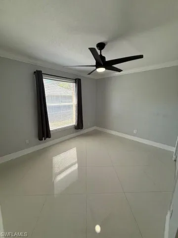 Empty room featuring crown molding, a ceiling fan, and light tile patterned floors