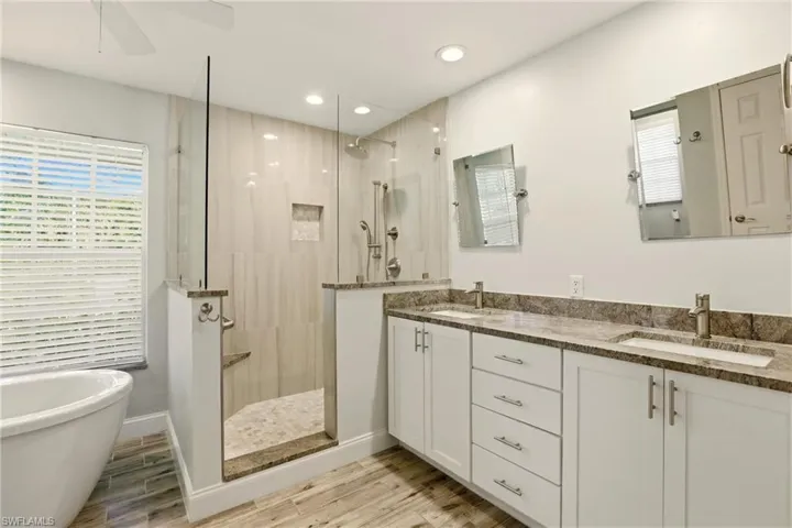 Full bath with double vanity, wood finish floors, a freestanding tub, a walk in shower, and a ceiling fan