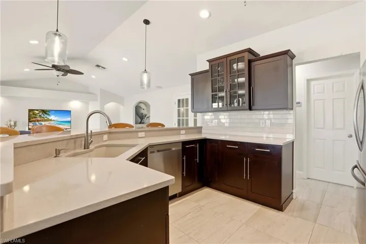 Kitchen featuring dark wood finish cabinetry, glass insert cabinets, a ceiling fan, pendant lighting, and lofted ceiling