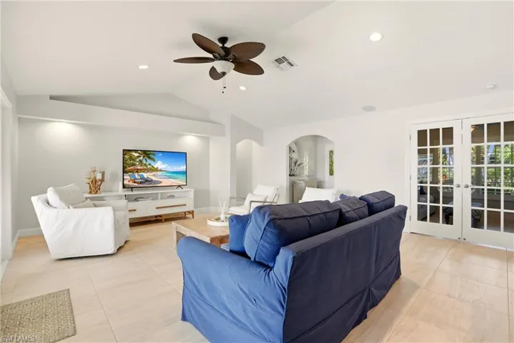 Living room featuring french doors, ceiling fan, arched walkways, light tile patterned floors, and vaulted ceiling