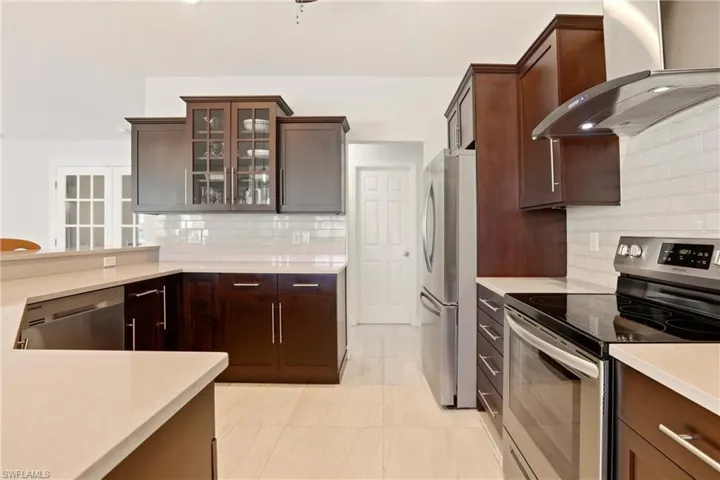Kitchen with stainless steel appliances, glass fronted cabinets, dark wood finish cabinetry, backsplash, and light stone countertops