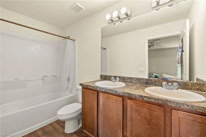 Bathroom with toilet, double vanity, shower / bathtub combination with curtain, wood finished floors, and ceiling fan