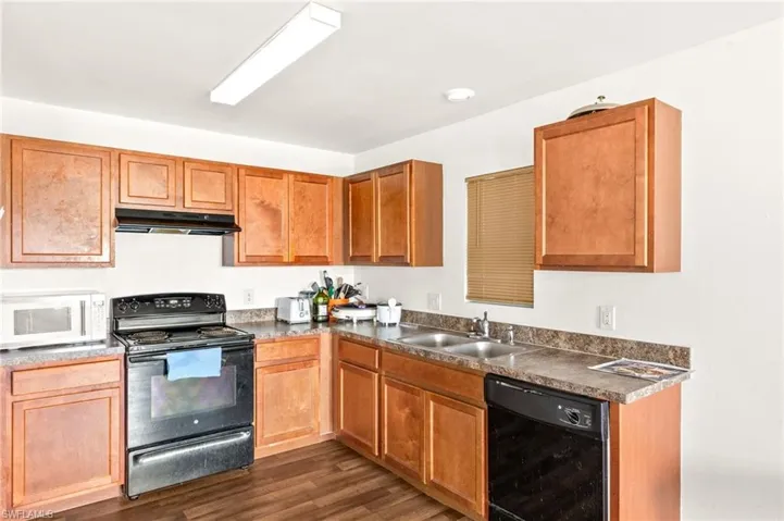 Kitchen featuring black appliances, a sink, under cabinet range hood, dark countertops, and dark wood finished floors