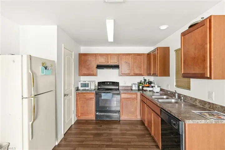 Kitchen with black appliances, a sink, dark wood-style flooring, under cabinet range hood, and dark countertops