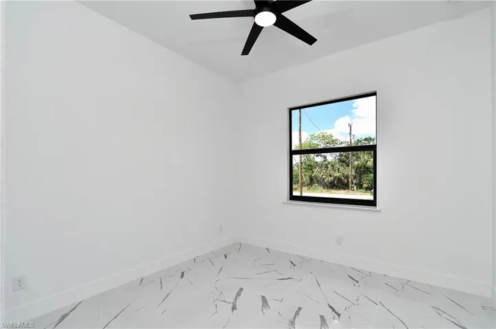 Bright interior space featuring a window with black trim, a ceiling fan, and white walls
