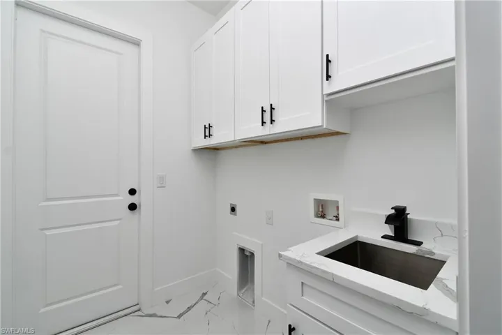 Dedicated utility space featuring white shaker-style cabinetry with matte black hardware, a stainless steel sink with a matte black faucet, and a countertop with subtle veining