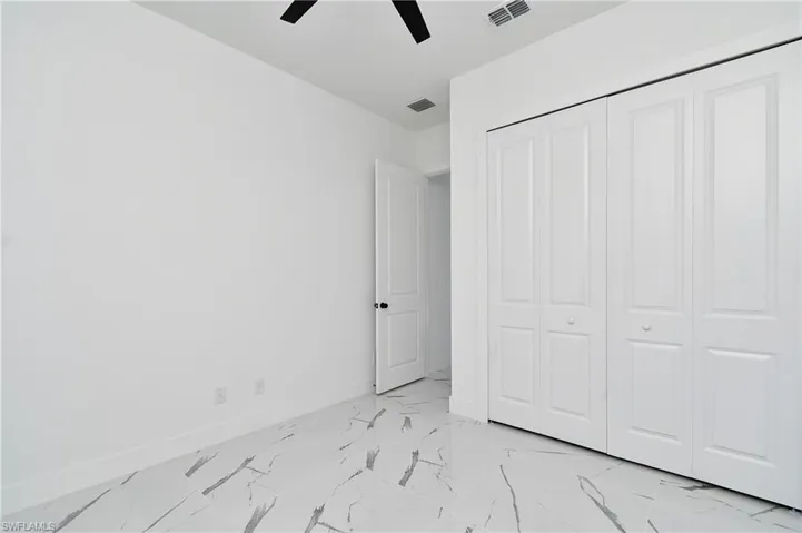 Room featuring large format tile flooring with distinctive veining, a ceiling fan with black blades, and a white bi-fold closet system
