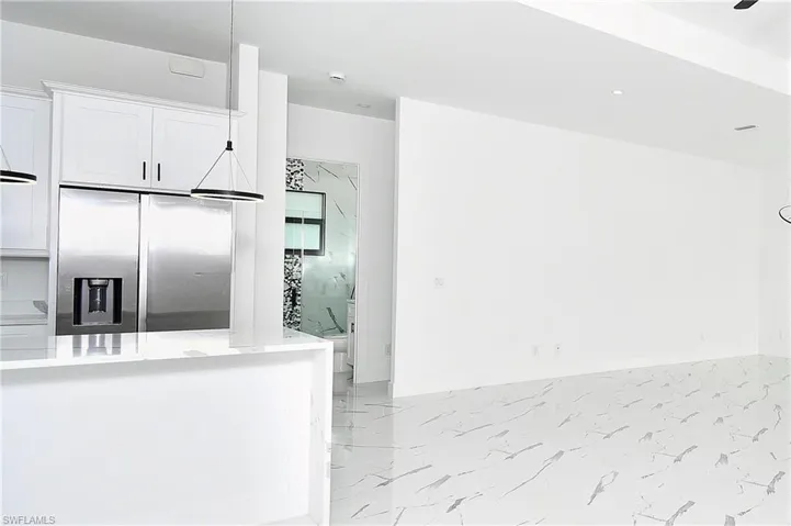 Bright kitchen area featuring white cabinetry, a stainless steel refrigerator, and a white countertop island