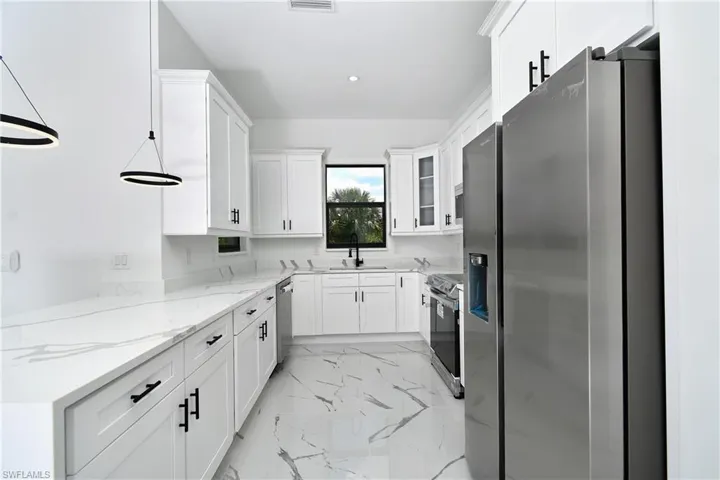 Contemporary kitchen featuring white cabinetry with black hardware, white countertops, stainless steel appliances, and large format floor tiles