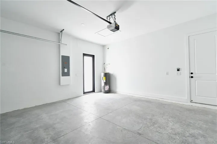 Spacious garage featuring a concrete floor, bright white walls, a side-entry door with a dark frame, and a white panel door