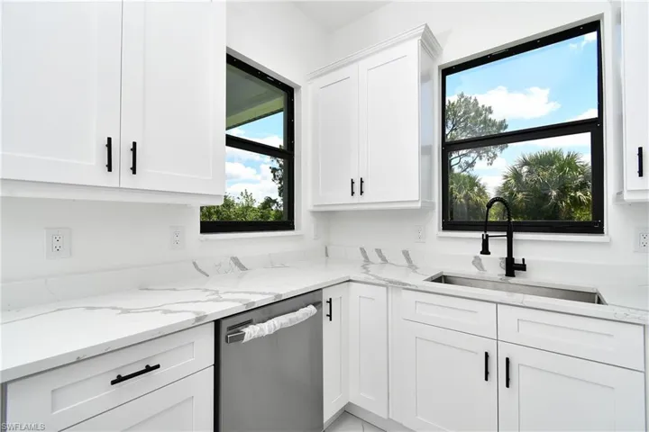 Modern kitchen featuring white shaker cabinetry with matte black hardware, white countertops with grey veining, a stainless steel undermount sink, and a black gooseneck faucet