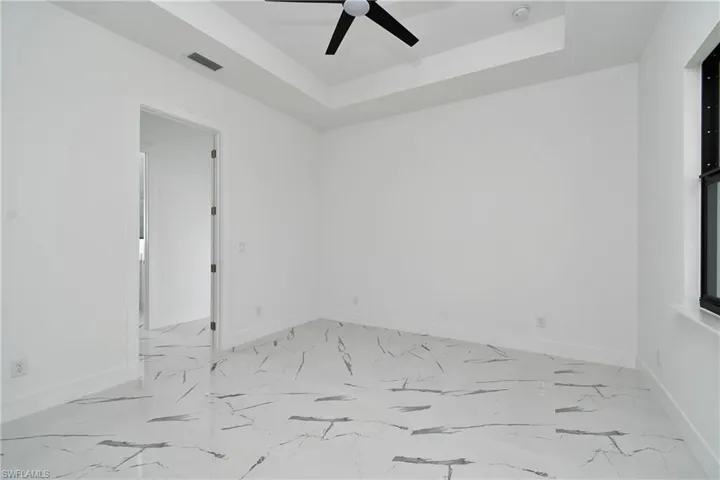 Spacious room featuring white walls, a tray ceiling with a black ceiling fan, and large format marble-look tile flooring