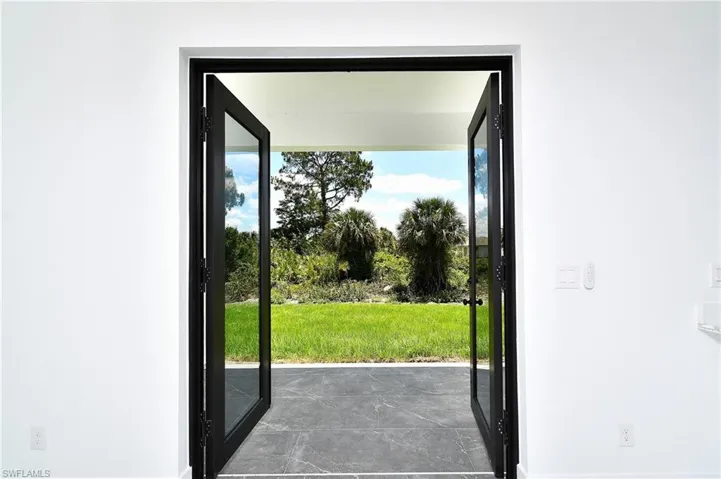 Black-framed glass French doors opening to an outdoor patio with dark tile flooring