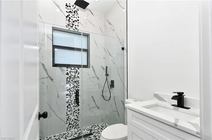 Glass-enclosed shower with a rainfall showerhead, large format marble-look tile, decorative mosaic tile accents, and a window