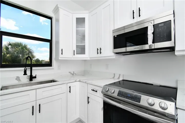 Kitchen featuring white shaker-style cabinetry, white countertops with gray veining, a stainless steel undermount sink with a matte black faucet, and a stainless steel over-the-range microwave