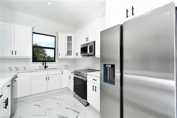 Modern kitchen featuring white cabinetry, stainless steel appliances, a black sink with a matching faucet, marbled flooring, and recessed lighting