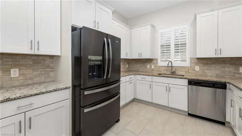 Kitchen with black fridge with ice dispenser, white cabinets, dishwasher, and light stone countertops