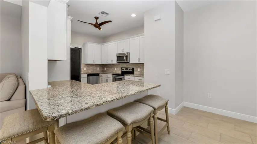 Kitchen featuring a peninsula, light stone countertops, tasteful backsplash, a breakfast bar area, and stainless steel appliances