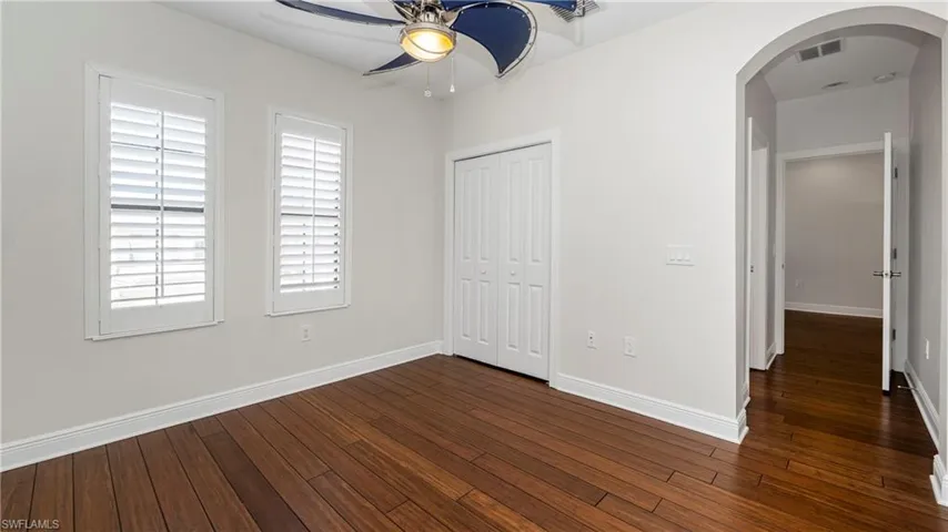 Unfurnished bedroom featuring arched walkways, dark wood-type flooring, a ceiling fan, and a closet