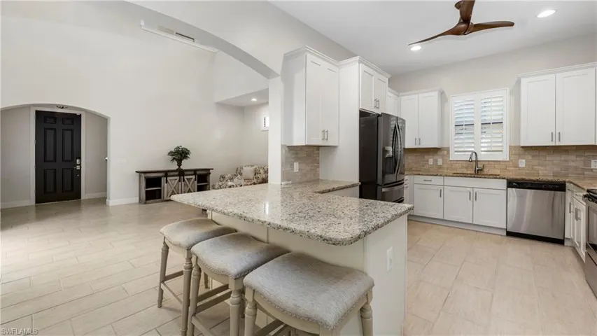 Kitchen featuring ceiling fan, arched walkways, light stone countertops, a breakfast bar area, and recessed lighting
