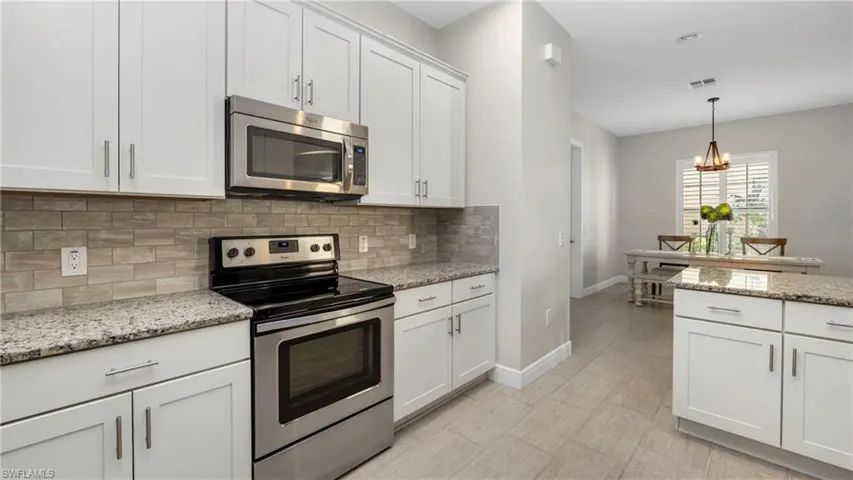 Kitchen with stainless steel appliances, white cabinetry, light stone countertops, and decorative backsplash